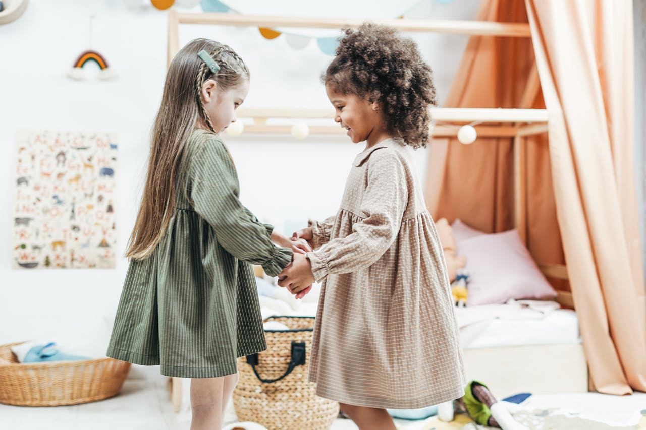 Two young girls holding hands and playing indoors, expressing joy and friendship in a cozy playroom.