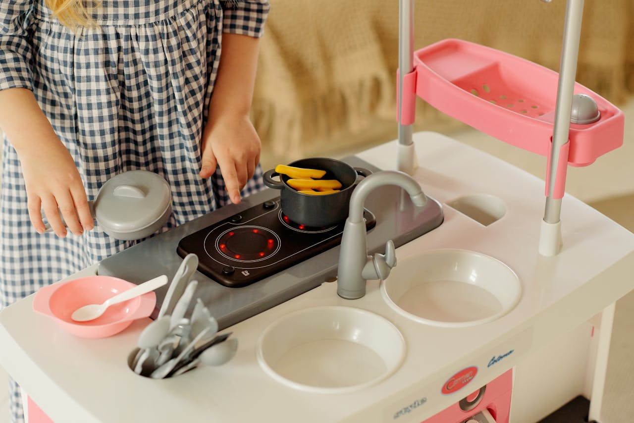 A young girl engaged in imaginative play with a toy kitchen set indoors. Perfect for concepts of childhood and creativity.