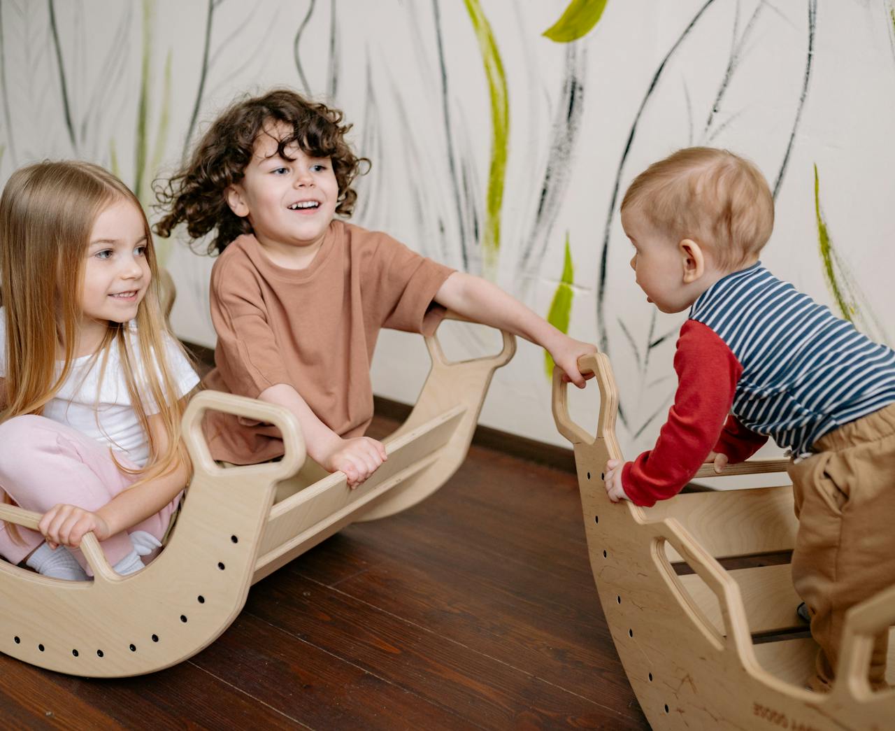 Three children enjoying playtime indoors on wooden rocking toys, smiling and engaging together.